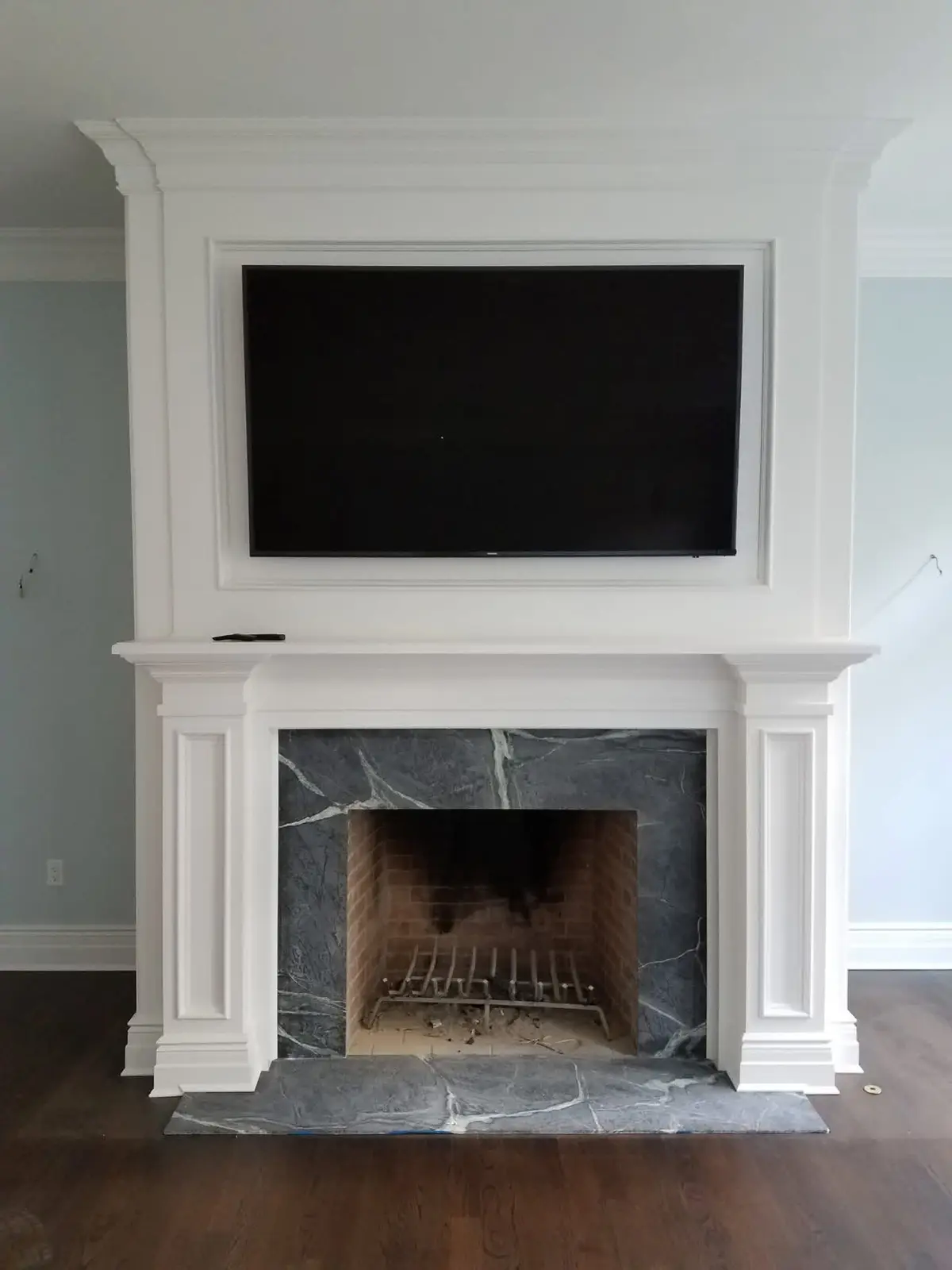 Custom white fireplace mantel with a mounted television and stone surround built by C&C Multiservices in Connecticut
