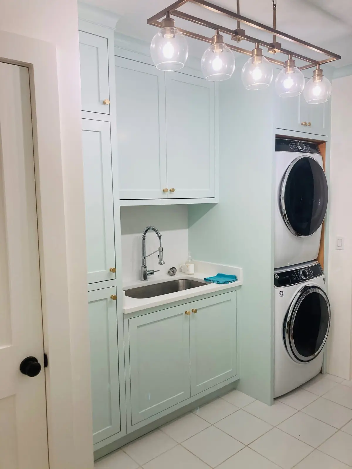 Custom laundry room with soft-green cabinetry, a farmhouse sink, and a stacked washer and dryer built by C&C Multiservices in Connecticut