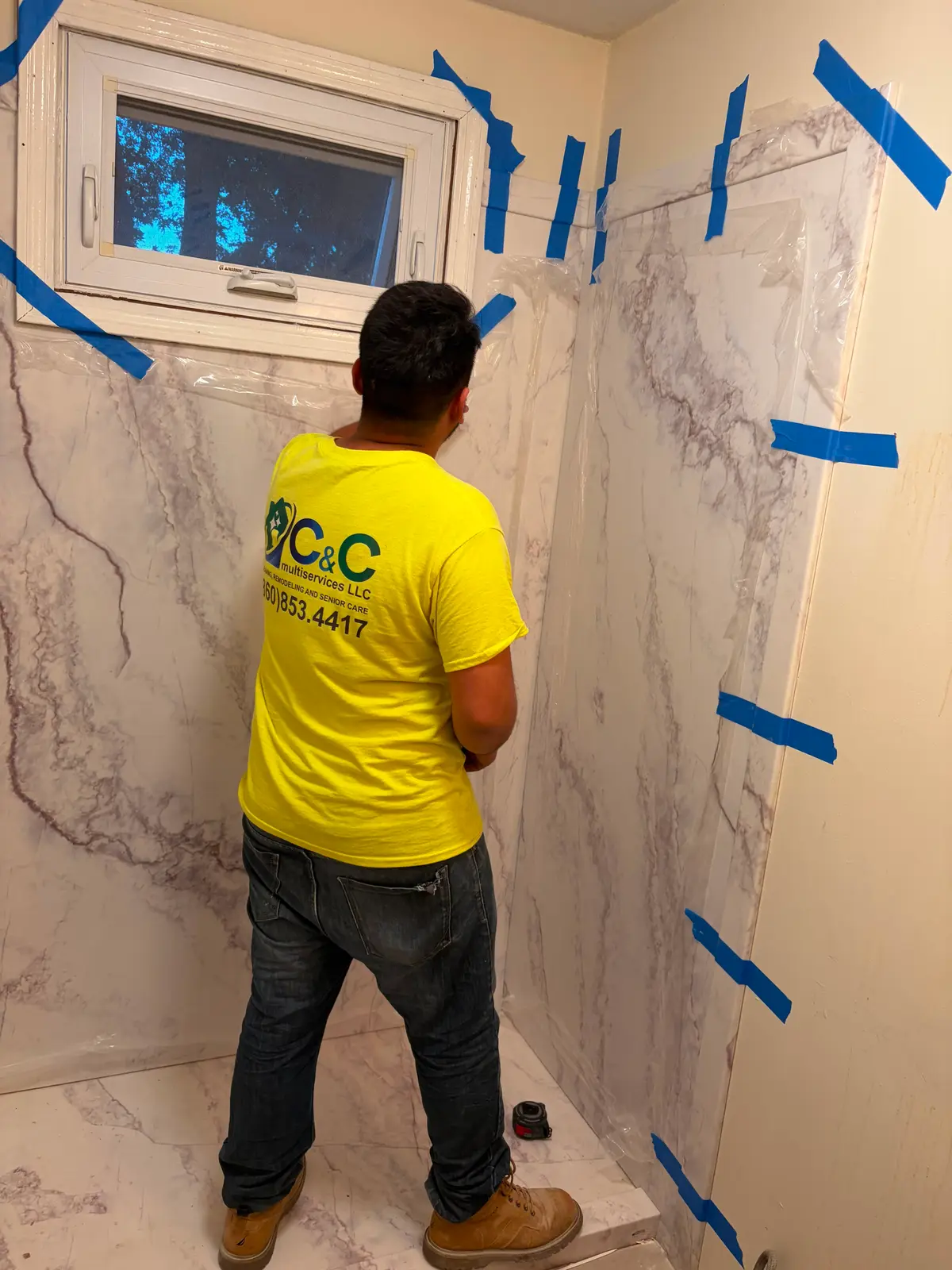 A C&C Multiservices team member in a branded company shirt installing a marble-look shower surround in Connecticut