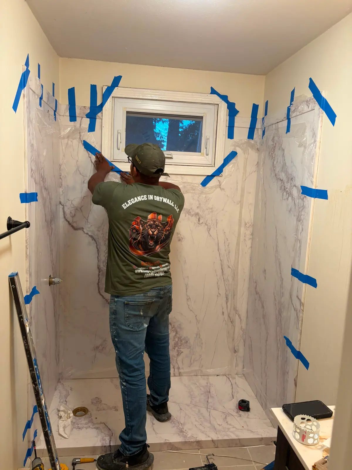 A contractor taping and sealing a marble-look shower panel on a C&C Multiservices project in Connecticut